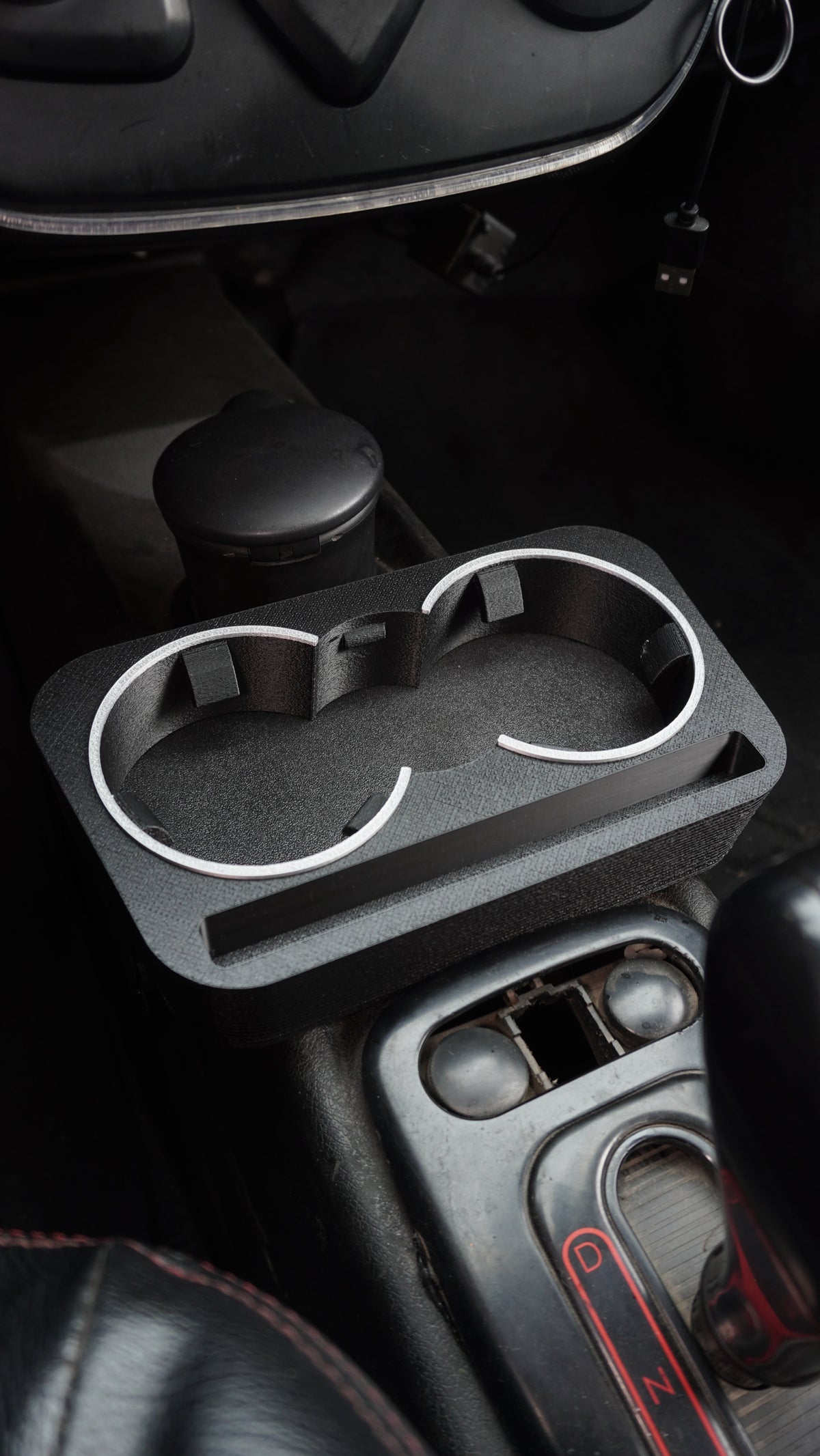 A black plastic dual cup holder tray with silver metal rims, mounted on a car's center console.