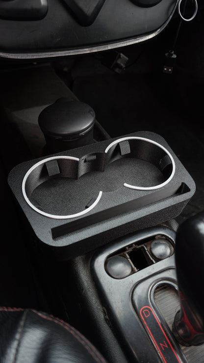 A black plastic dual cup holder tray with silver metal rims, mounted on a car's center console.