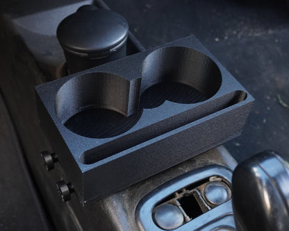 A black dual cup holder organizer tray mounted on a car center console next to the gear shift knob.