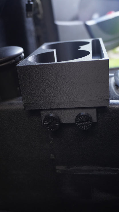 A dark gray textured cup holder mount with two circular cup holders, shown mounted on a black surface with two black knobs below.