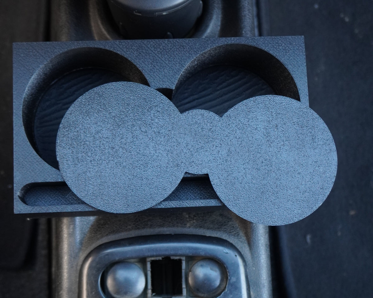 A gray dual circular cup holder insert with a textured foam-like finish, shown installed into a black plastic car center console cup holder.